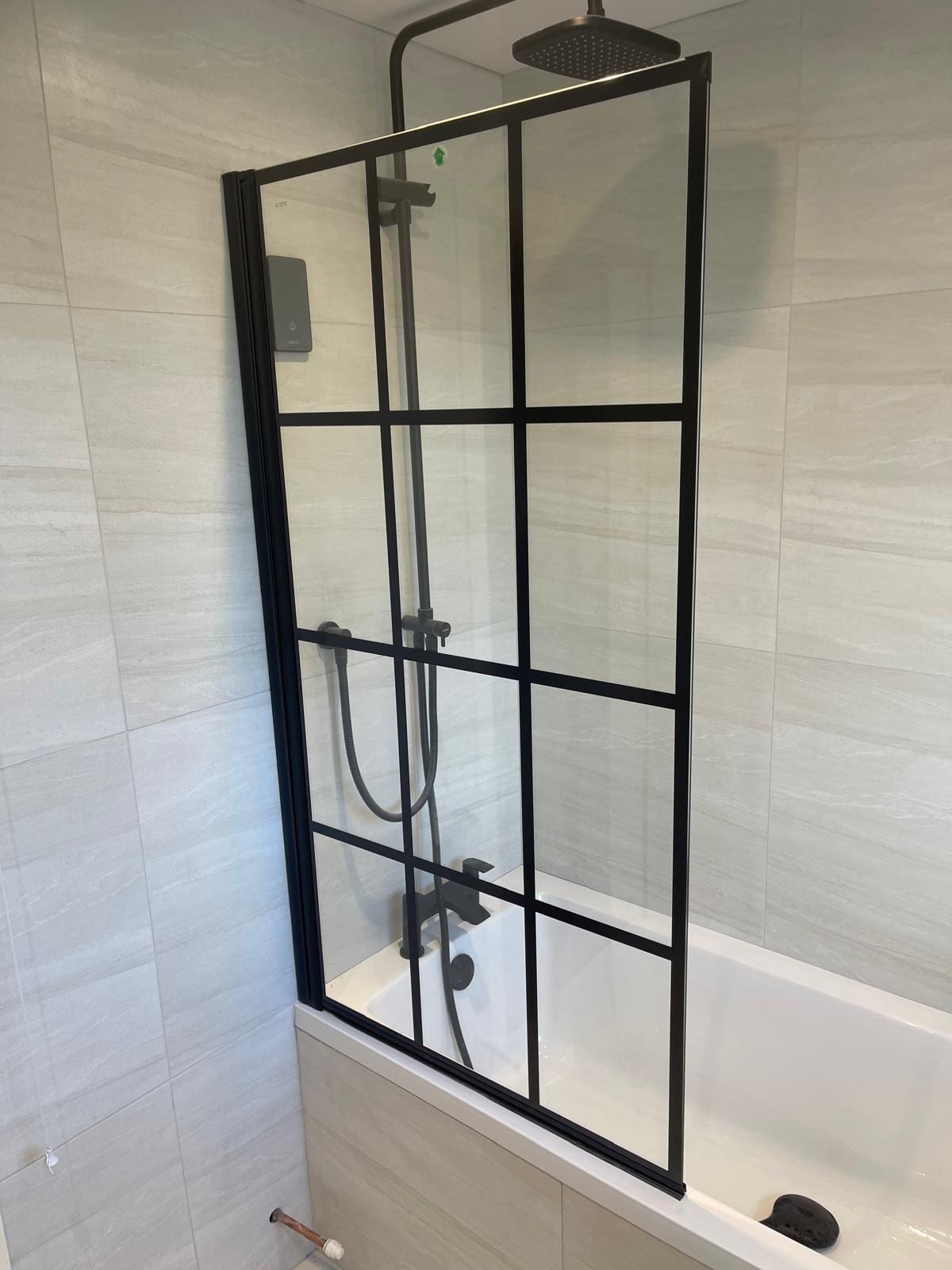 Bath with black framed grid shower screen, matt black shower valve and light stone-effect tiles
